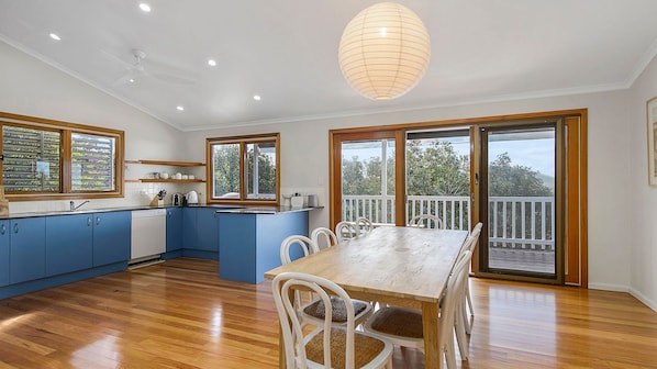 A modern kitchen with blue cabinets, a wooden dining table, and a balcony with a view.