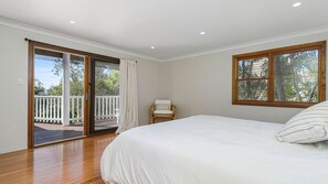 Un dormitorio con una cama grande, una silla, una puerta corrediza de vidrio que da a una terraza exterior y una ventana con vistas a árboles.