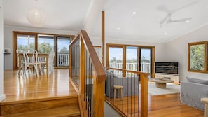 A spacious living area with a wooden staircase, a dining area with chairs, a sofa, and a television.