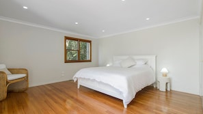 A bedroom with a large bed, a window, a chair, and a bedside table with a lamp.