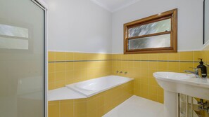 Un baño con bañera, lavamanos y paredes con azulejos amarillos.