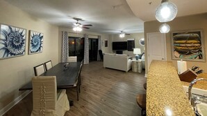 Amplia sala de estar con mesa de comedor, sillas, cocina con encimera de granito y ventilador de techo.