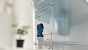 Ein Wasserhahn mit klarem Wasser, einer blauen Ausgießdüse und einem transparenten Behälter.