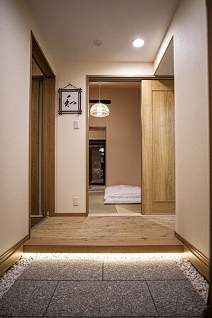 A hallway with wooden flooring, a small rug, a hanging light fixture, and a framed picture on the wall.