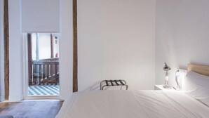 Un dormitorio con cama, mesita de noche, lámpara y vistas a un balcón con suelo a cuadros.
