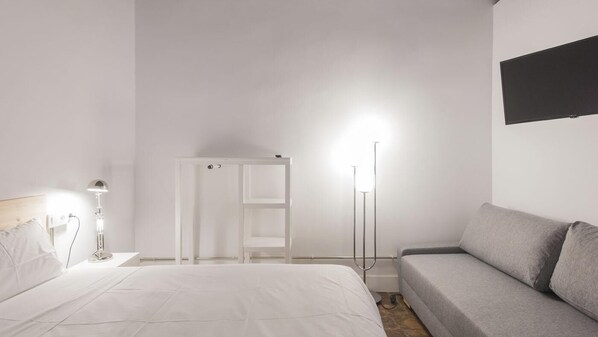 A bedroom with a bed, a grey sofa, a white wardrobe, and a floor lamp.
