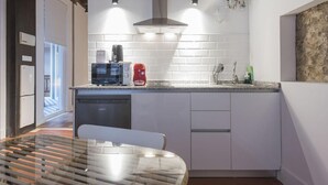 Una cocina moderna con azulejos blancos tipo metro, horno empotrado, cafetera y hervidor rojo.