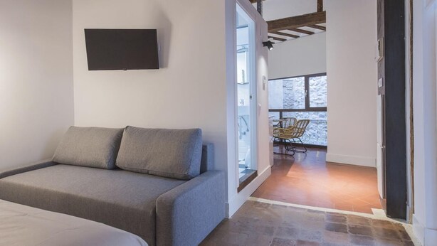 Una habitación moderna con un sofá gris, un televisor de pantalla plana montado y vistas a una terraza de madera con sillas.