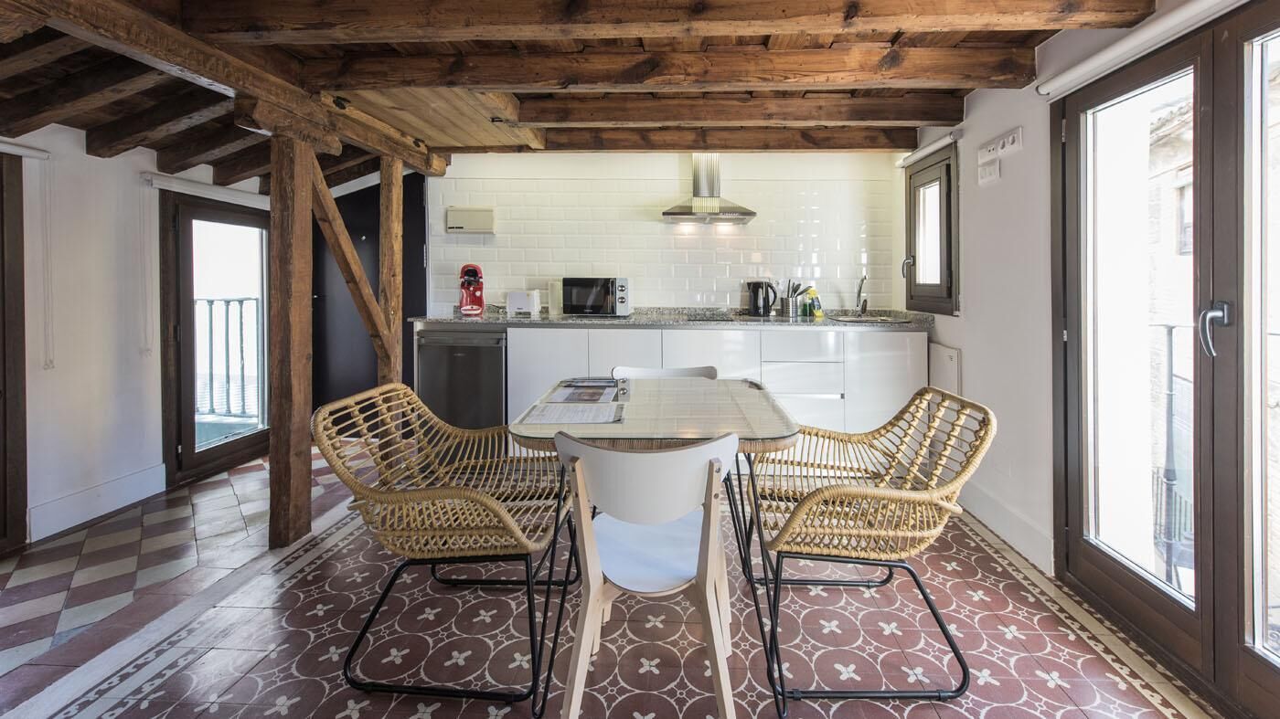Una cocina con una mesa de comedor y sillas de mimbre, suelo de baldosas y techo de madera.