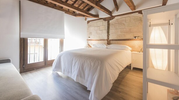 Un dormitorio con una cama grande, vigas de madera, pared de piedra y vistas a través de una ventana.