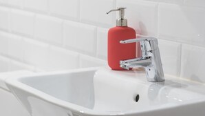 Un lavamanos blanco con grifo cromado y dispensador de jabón rojo.