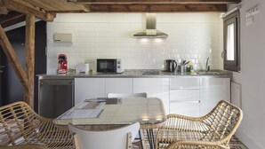 Cocina compacta con azulejos blancos, microondas, hervidor y comedor con sillas de mimbre y mesa de vidrio.