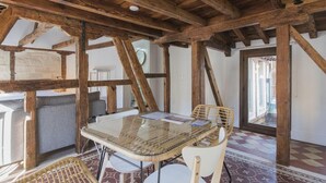 Un interior rústico con vigas de madera a la vista, una mesa de vidrio, sillas de mimbre y un suelo estampado.