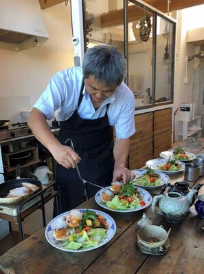 Un chef prepara comida en una cocina con mesas de madera y un amplio ventanal.
