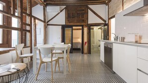 Una cocina con piso a cuadros, vigas de madera, gabinetes blancos y un comedor con sillas y una mesa.