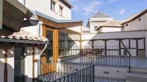 Un patio con una pérgola de madera, una mesa con sillas y vistas a edificios tradicionales.