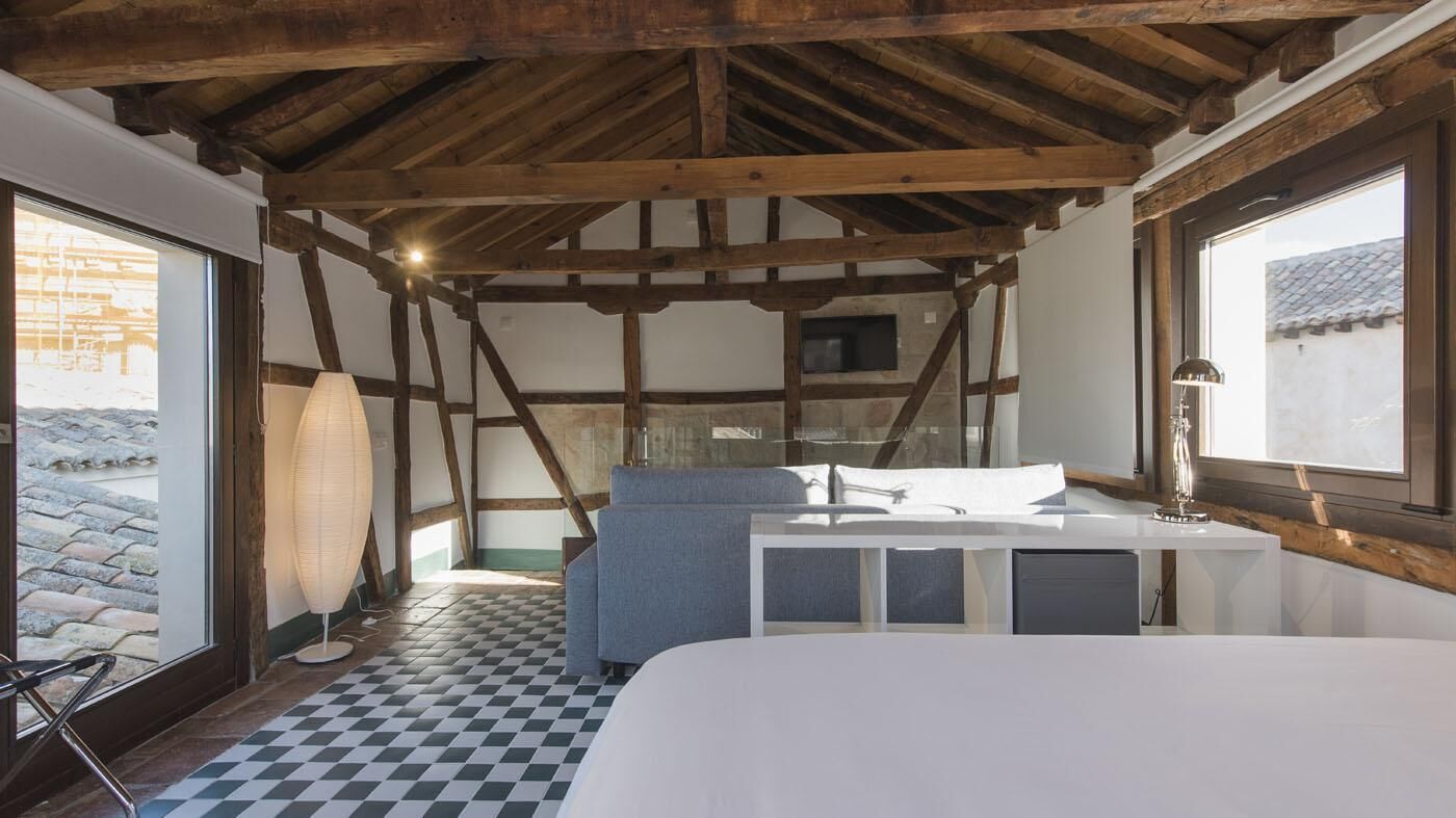 A bedroom with a checkered floor, a bed, a sofa, a desk, and a window with a view of the outside.