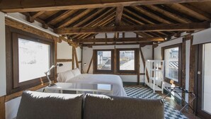 Un dormitorio con techo de madera, una cama, un escritorio y una ventana con vista a edificios.
