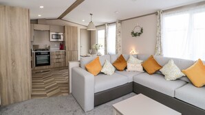 Una sala moderna con un sofá gris, una mesa de centro blanca y una cocina al fondo.