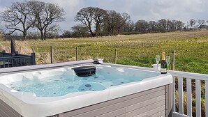 Un jacuzzi en una terraza al aire libre con vista a un campo de hierba y árboles en el fondo.