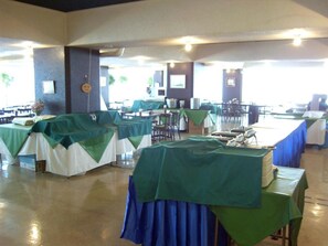 Un salón de banquetes con mesas cubiertas con manteles verdes y blancos, dispuestas en filas.