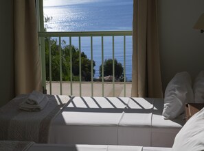 Une chambre avec un lit, une vue sur la mer et un balcon doté d’une balustrade.