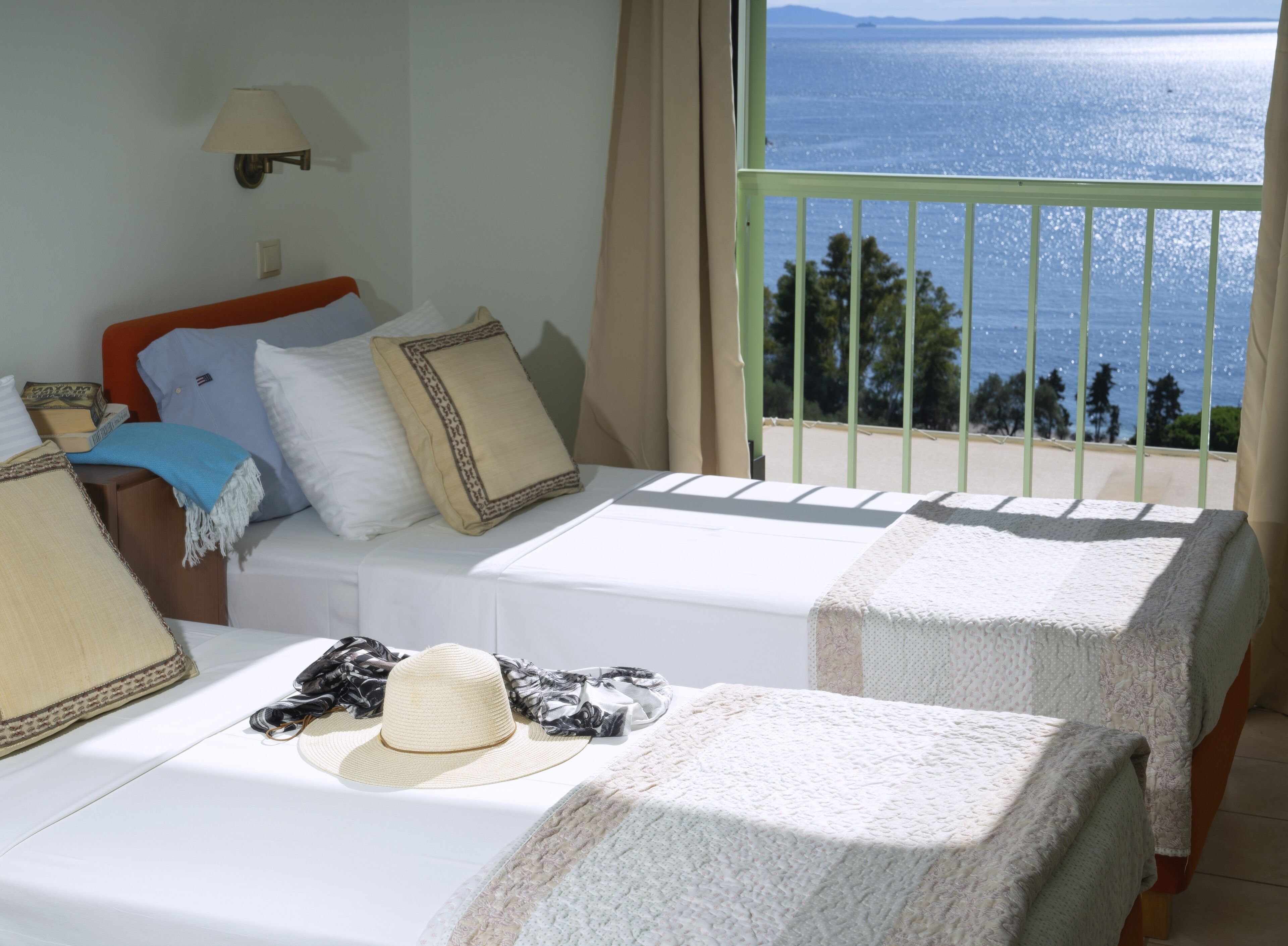 Hotelkamer met twee bedden, uitzicht op zee en een balkon met een hekwerk.