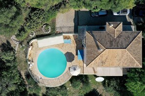 An aerial view of a property with a swimming pool, a covered patio, and a multi-level roof structure.