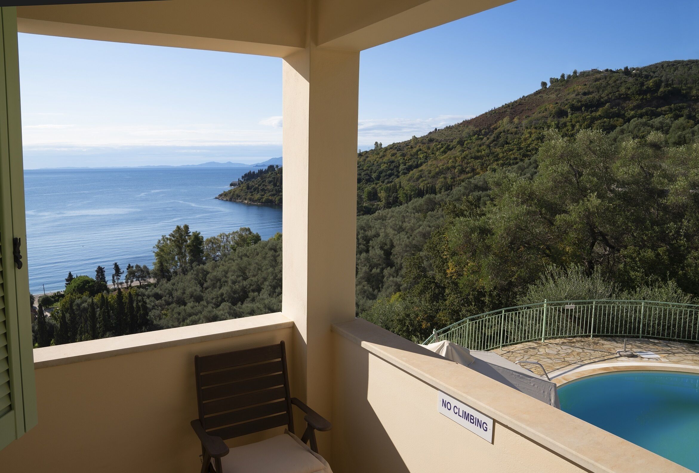 Un balcon avec vue sur un lac et des collines, un espace piscine avec un panneau indiquant « Il est interdit de grimper », et une chaise.