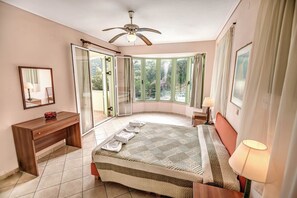 A bedroom with a bed, a desk, a chair, a ceiling fan, and a large window with curtains.
