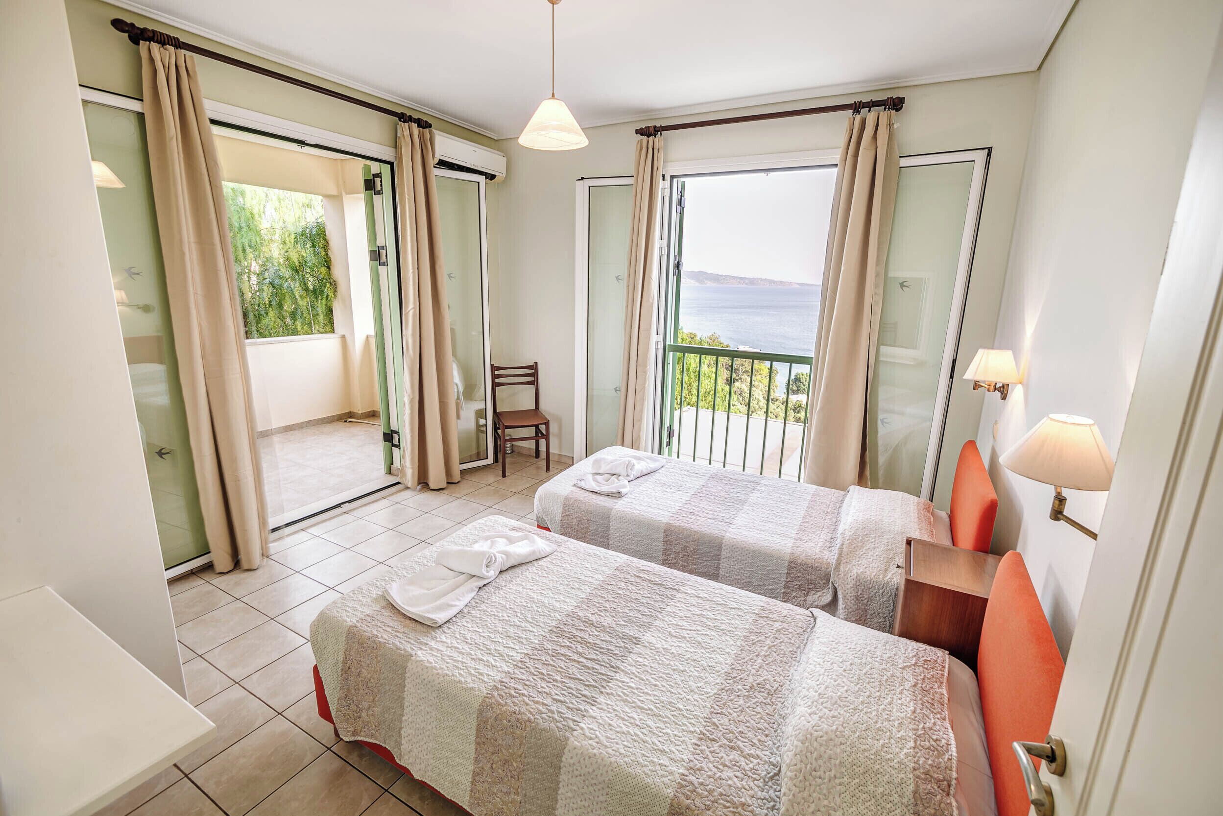 Habitación de hotel con dos camas, una silla, una mesa y un balcón con vistas.