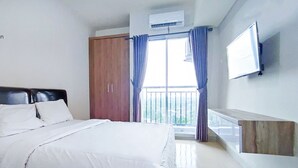 A hotel room with a bed, a wardrobe, a balcony with curtains, and a mounted TV. - Apartmen Serpong GreenView byRuangNyaman (South Tangerang)