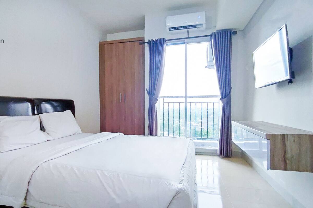Una habitación de hotel con cama, armario, balcón con cortinas y televisor montado.