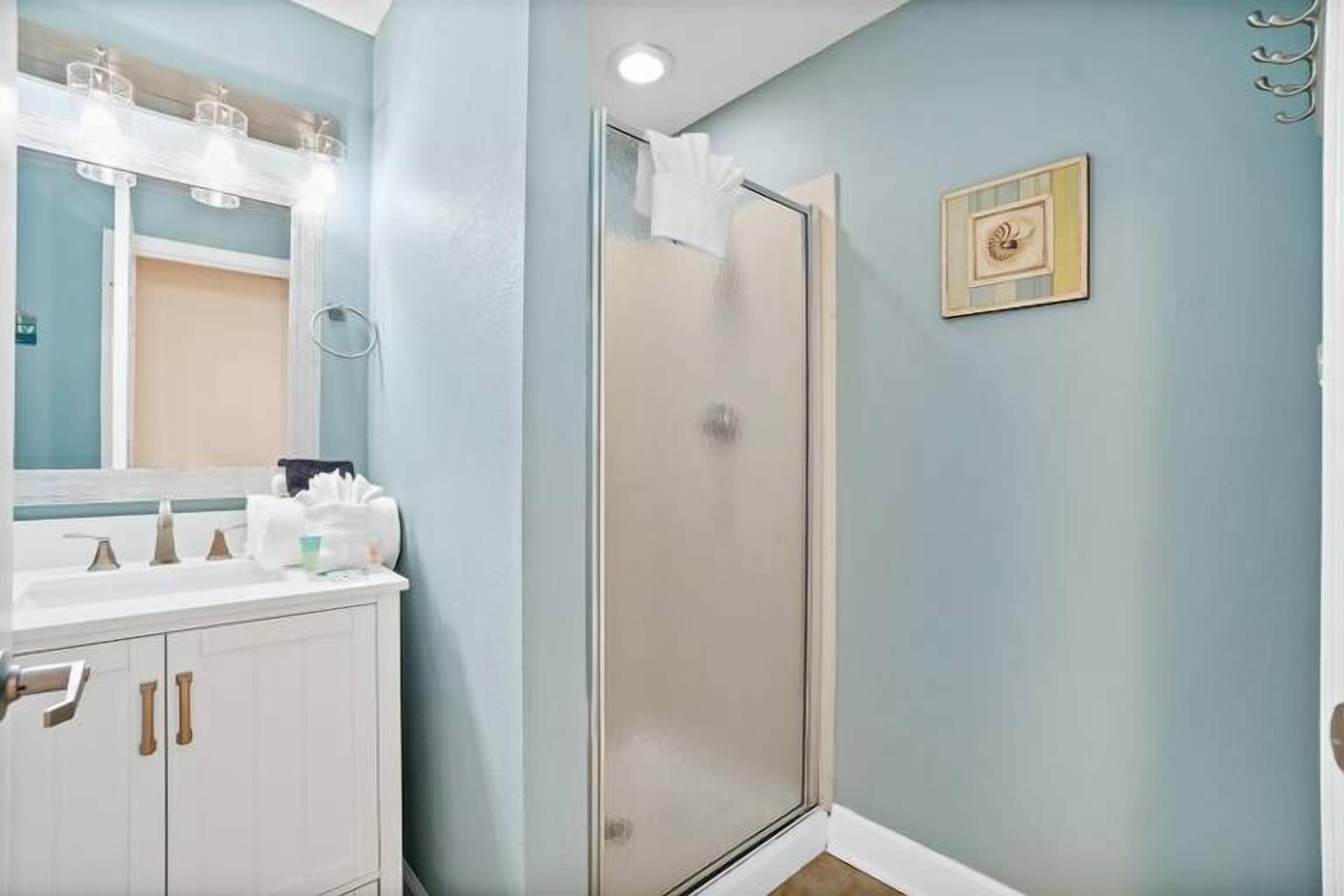 Un baño con tocador blanco, cabina de ducha con mampara de vidrio y un cuadro en la pared.