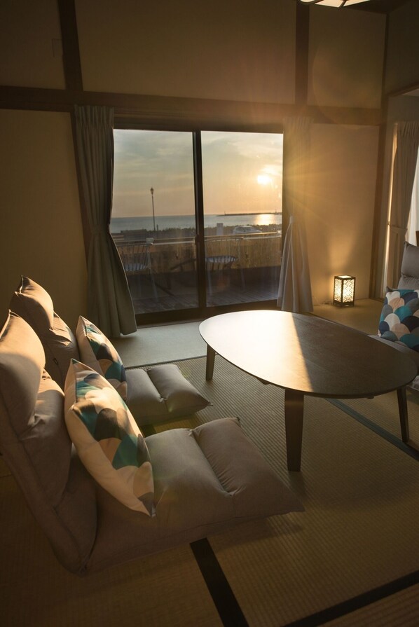 Una habitación con sofá, una pequeña mesa redonda y vista al atardecer a través de un ventanal.