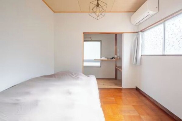 Un dormitorio con cama, suelo de madera, lámpara con diseño geométrico, ventana con cortinas estampadas y estante empotrado.