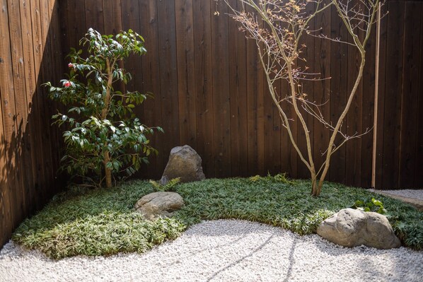 Un jardin entouré d’une clôture en bois, un arbre aux feuilles vertes et un jardin de rocaille avec du gravier et de l’herbe.