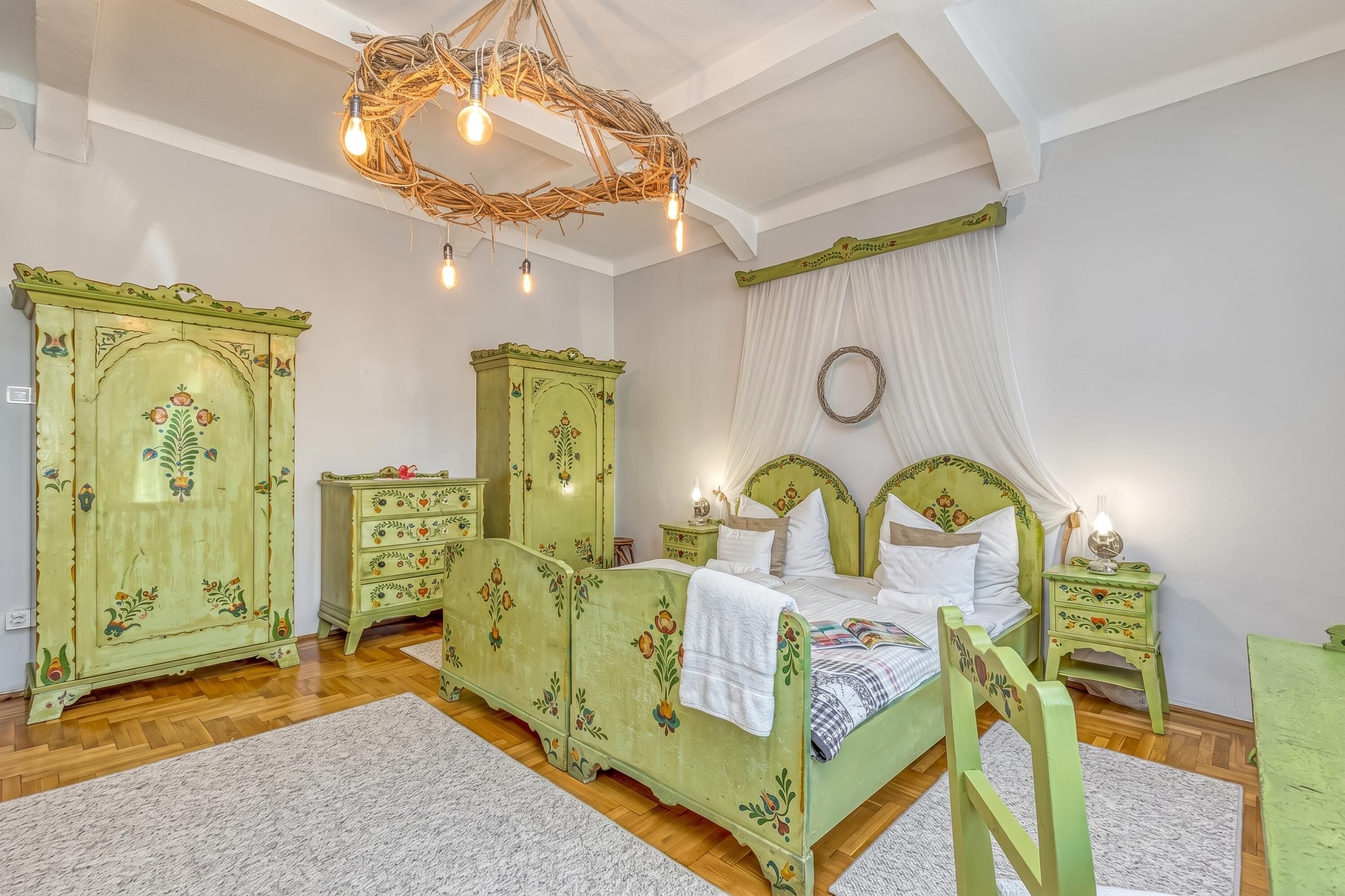 A room with a bed, two nightstands, a dresser, and a chandelier.