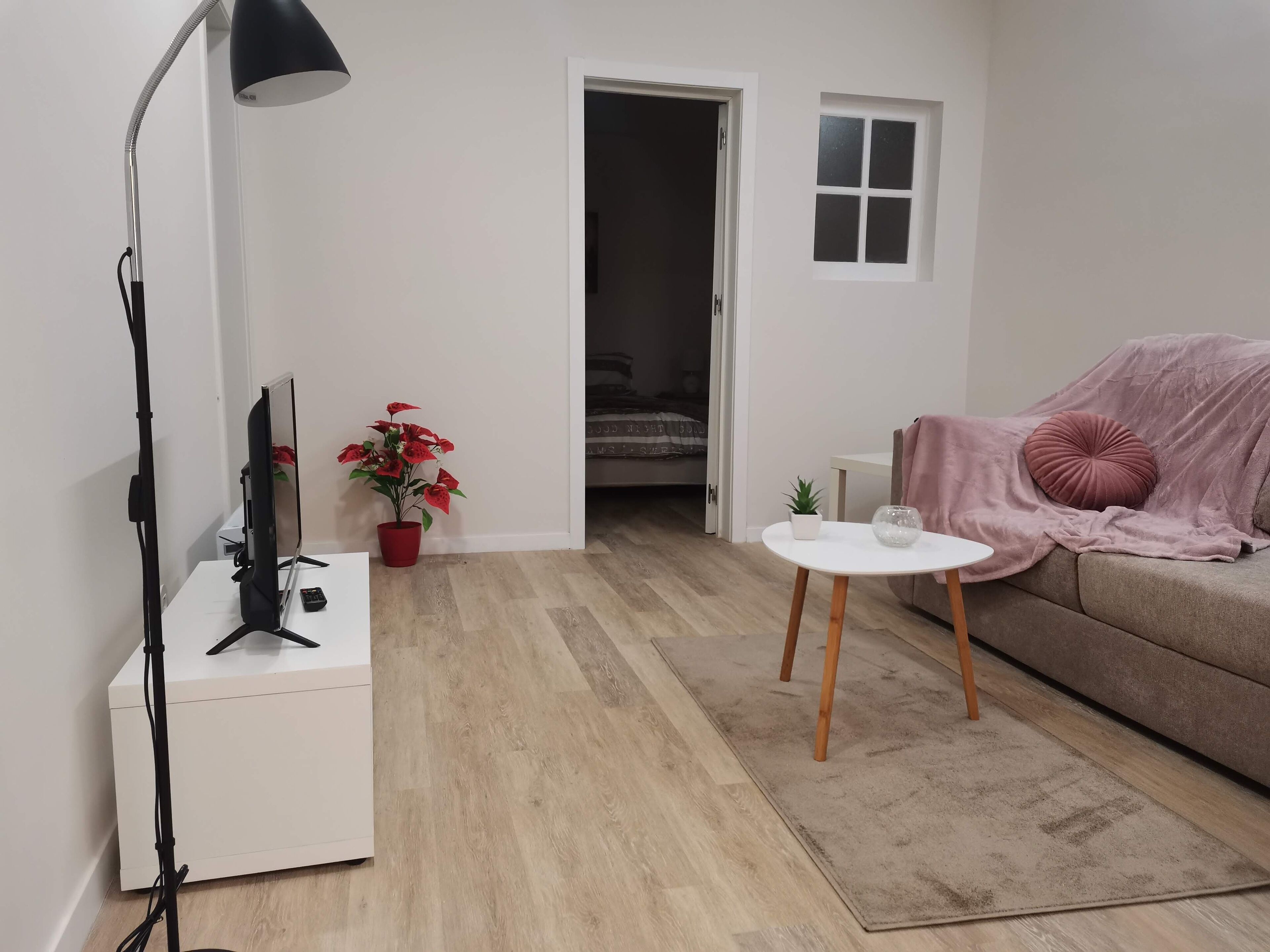 Una sala de estar moderna con un sofá blanco, una pequeña mesa blanca, una planta en maceta roja y una lámpara de pie negra.