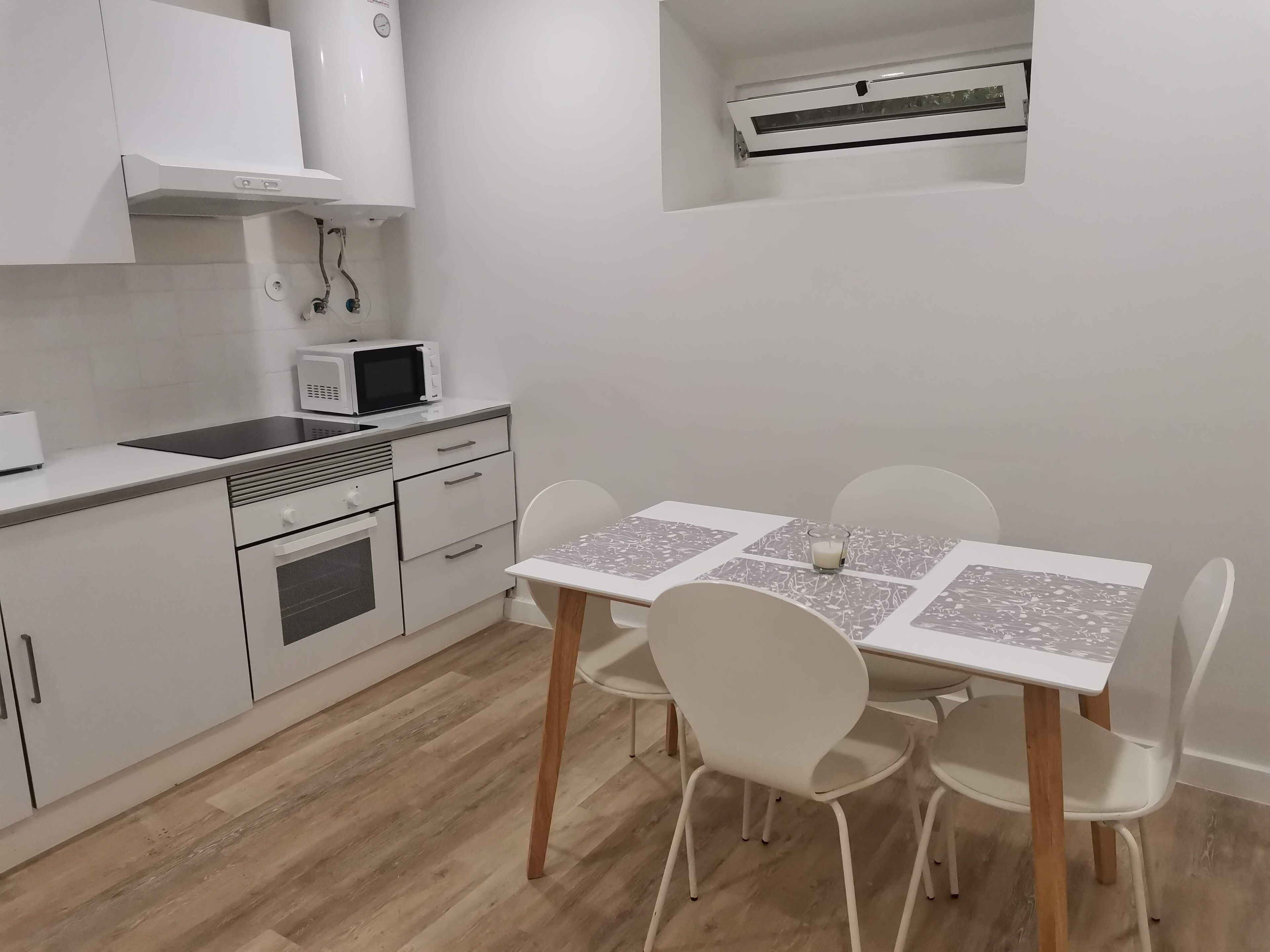 Una cocina compacta con armarios blancos, un microondas y una pequeña mesa de comedor con sillas.