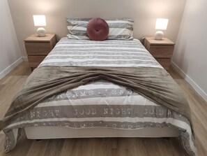 Una cama bien hecha con un edredón a rayas, dos lámparas de noche y una almohada rosa.