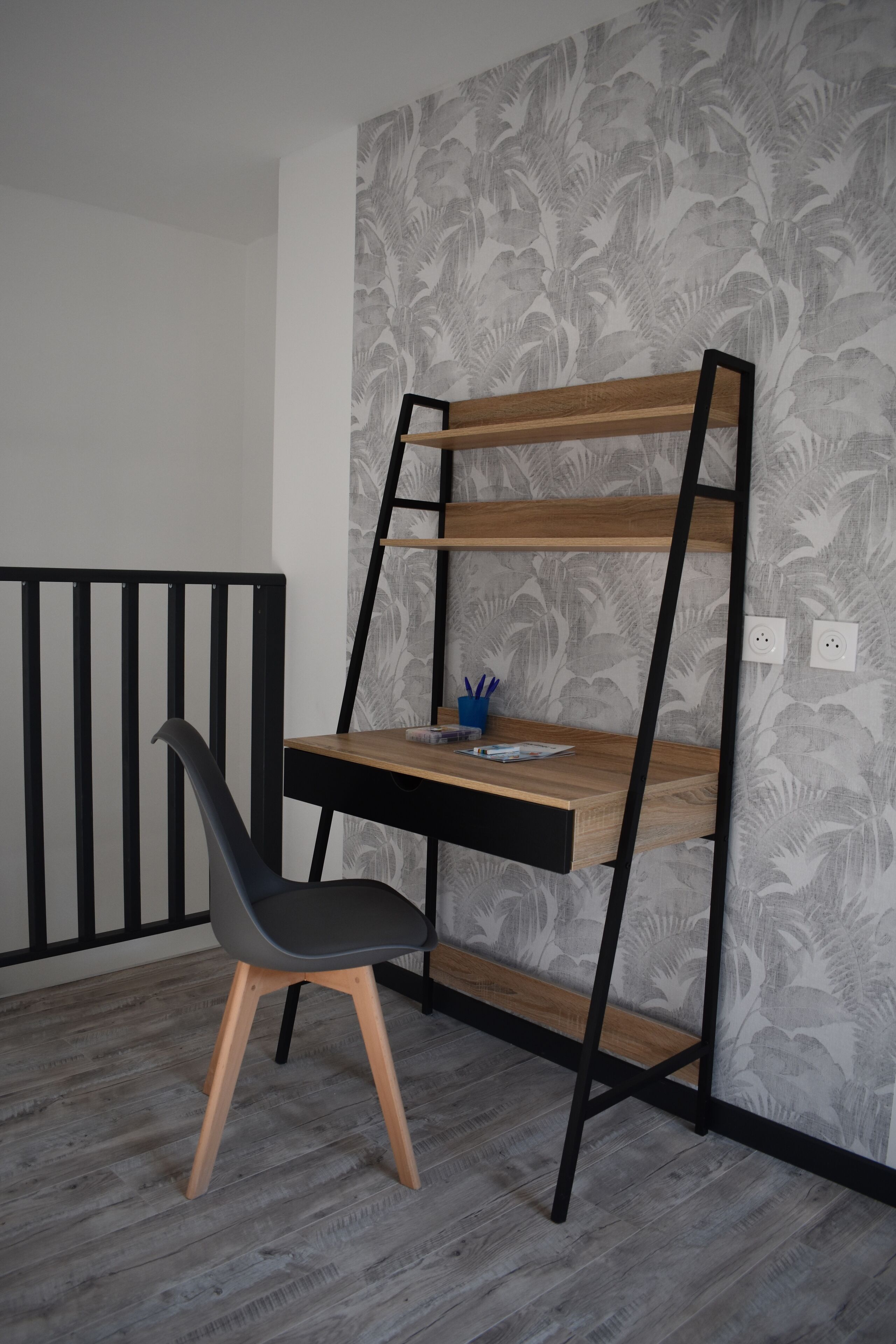 Una habitación con un escritorio junto a la pared, una silla y una barandilla negra.