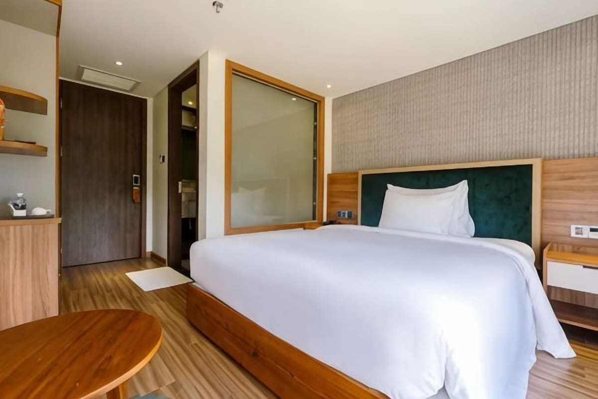 A hotel room with a large bed, a wooden desk, and a door leading to a bathroom.