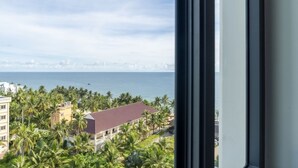 Vista desde una ventana con vista a una zona costera, palmeras y el perfil de una ciudad a lo lejos.