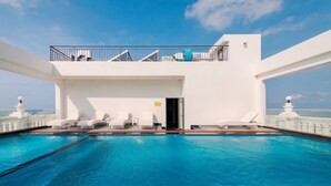 Un área de piscina con sillas reclinables blancas y un balcón con barandilla.