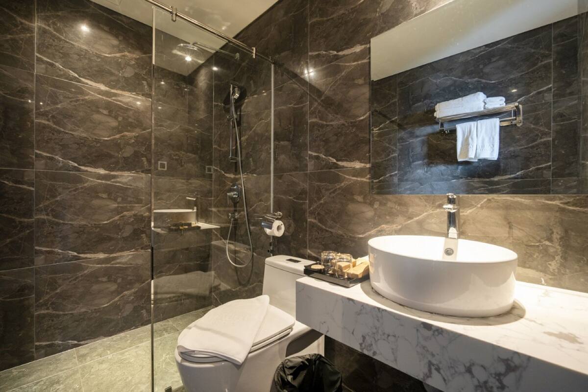 Une salle de bain moderne avec un mur en marbre, une cabine de douche en verre, un lavabo blanc et un porte-serviettes.
