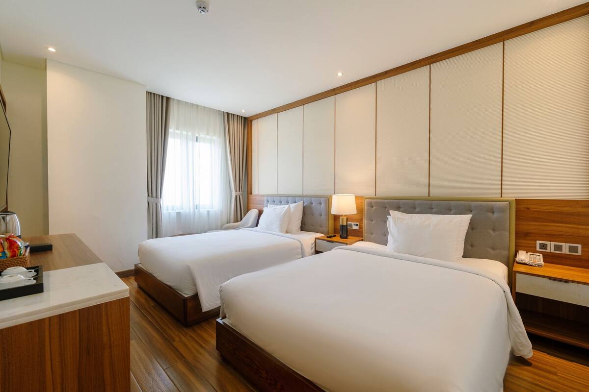 Une chambre d’hôtel avec deux lits, un bureau en bois, un téléphone et une fenêtre avec des rideaux.