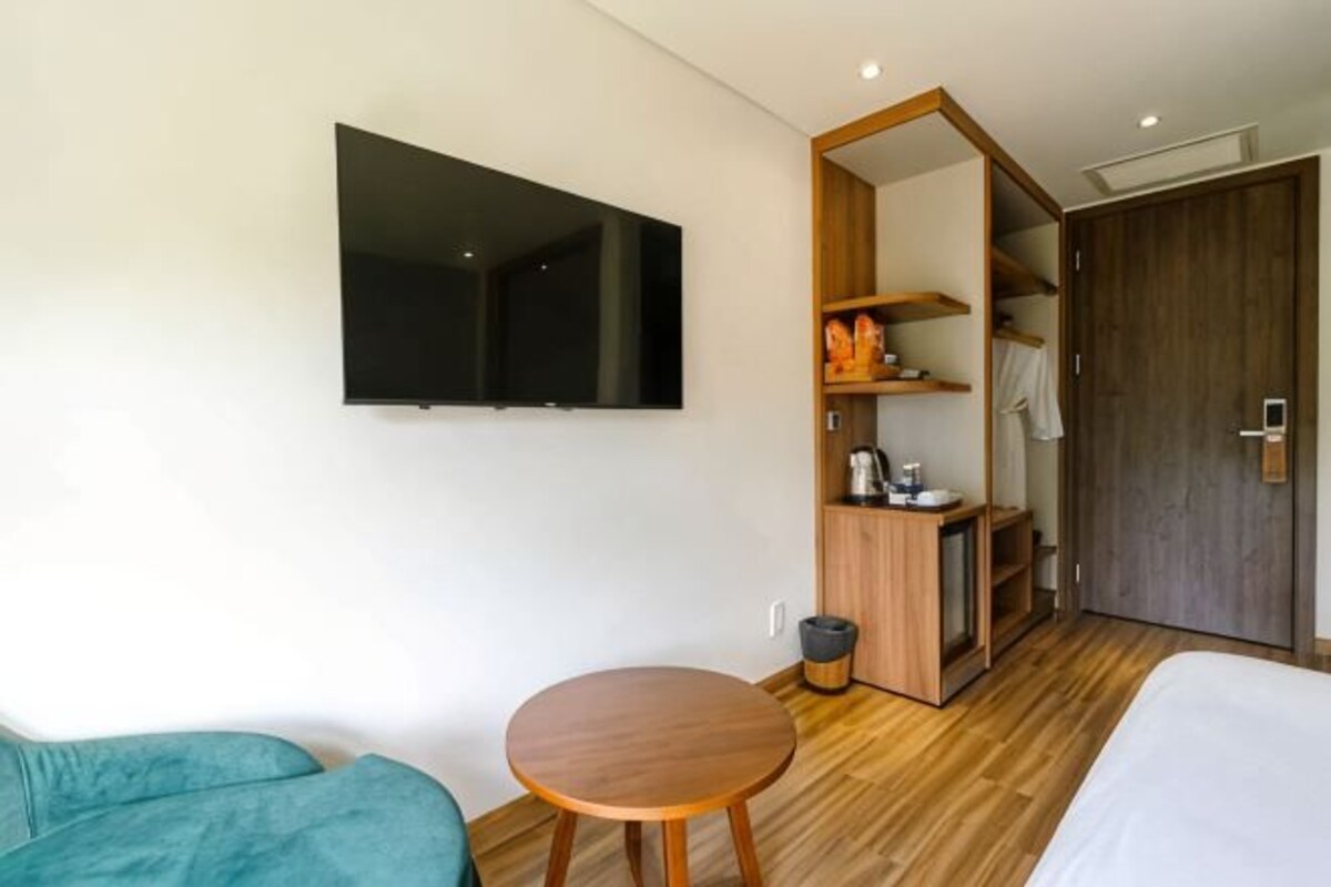 Ein Hotelzimmer mit einem Bett, einem runden Holztisch, einem an der Wand montierten Fernseher, einem Kleiderschrank und einer kleinen Küchenzeile.