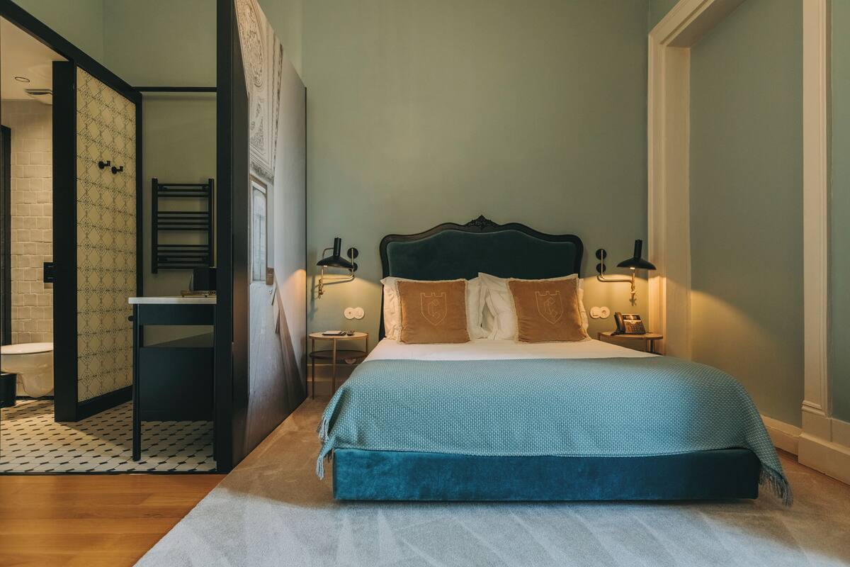 A bedroom with a bed, bedside tables, a nightstand, a mirror, and a door leading to a bathroom.