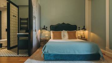 Une chambre à coucher comprenant un lit, des tables de chevet, une commode, un miroir et une porte donnant accès à une salle de bain.